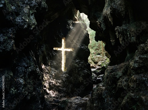 Sunlight streams through a cave opening illuminating a cross shape.
