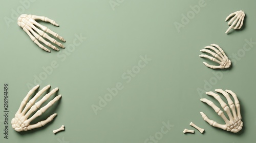 Flat lay composition of multiple human skeleton hands arranged on a solid sage green background for halloween