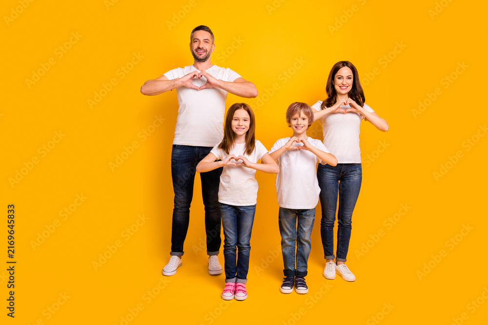 Fototapeta premium Happy family portrait with parents and two children making heart hands on bright yellow background, casual clothing and smiling together to show love and unity