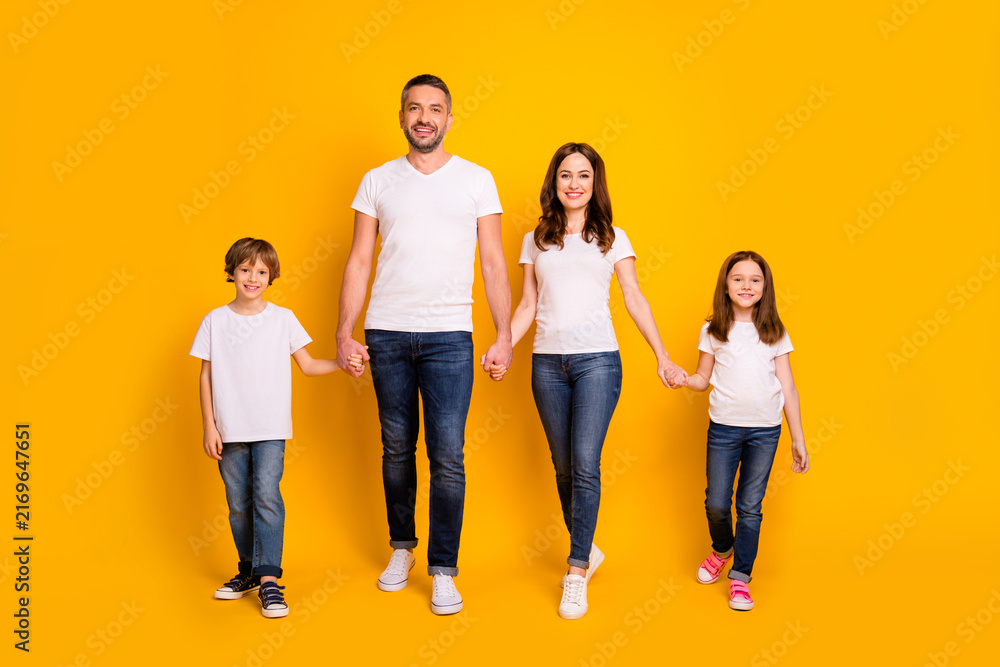 Obraz premium Happy family of four holding hands and smiling against a bright yellow background, parents with two children in casual white t-shirts and jeans