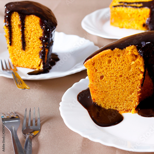 Slice of brazilian carrot cake with chocolate frosting served on a white plate, with other slices in the background
