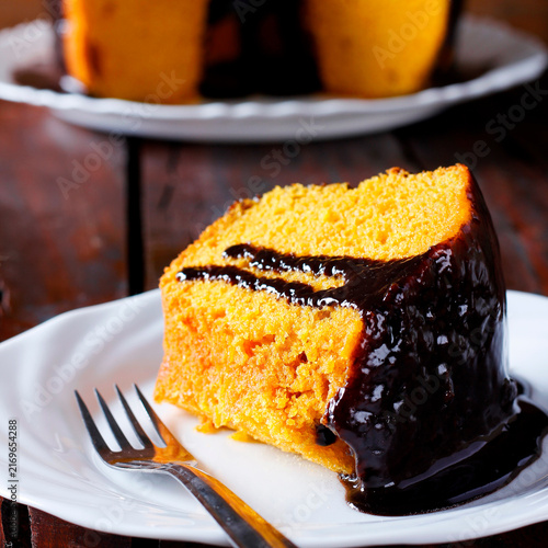 Slice of carrot cake with generous chocolate frosting on a white plate.
