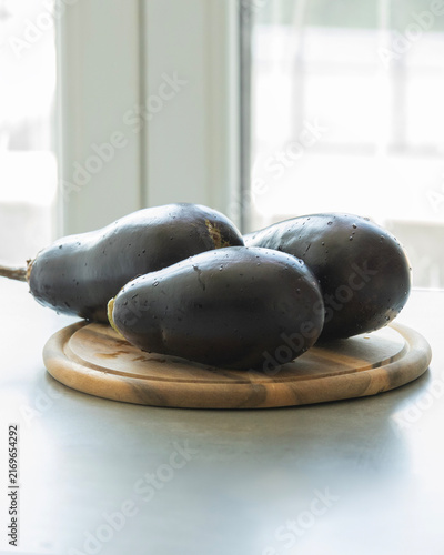 Three Fresh Purple Eggplants Stacked on Wooden Cutting Board Close Up