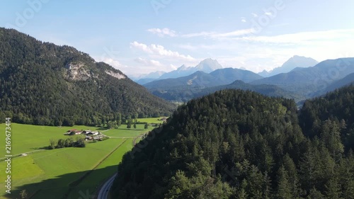 Aerial drone view of a scenic mountain road winding through dense forests and green alpine landscapes near Bischofswiesen, Bavaria, Germany. Drone footage with a calm and relaxing atmosphere.