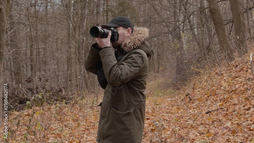 man photographing fallen leaves in the forest with a focused and concentrated side view of wooden trees and dry nature in brown and green tones, outdoor activities.