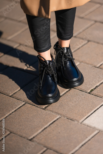 Obraz na plátně black leather boots standing on urban sidewalk close-up of feet casual and stylish fashion street style market context natural light clean background copy space editorial educational visual