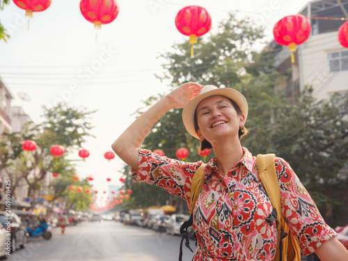 Young woman traveler walks down lively street in Bangkok during Chinese New Year. Festive atmosphere, colorful decorations, paper lanterns, and busy city life surround tourist.
