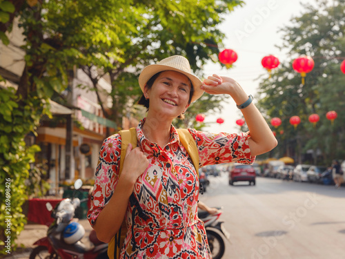 Young woman traveler walks down lively street in Bangkok during Chinese New Year. Festive atmosphere, colorful decorations, paper lanterns, and busy city life surround tourist.