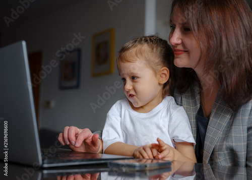 mother with a child sits at a table and works on a laptop. remote work mom baby concept. Work-from-home mom focused on her laptop, managing online tasks while balancing motherhood and career.
