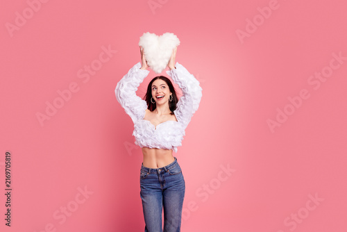 Фотография Young woman holding fluffy heart pillow above her head on pink background smilin