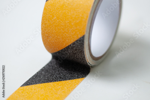 Bild auf Leinwand Roll of black and yellow anti-slip safety tape with diagonal hazard stripes on a white background