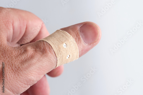 Male thumb wrapped with fabric adhesive bandage plaster for first aid care and minor injury protection.