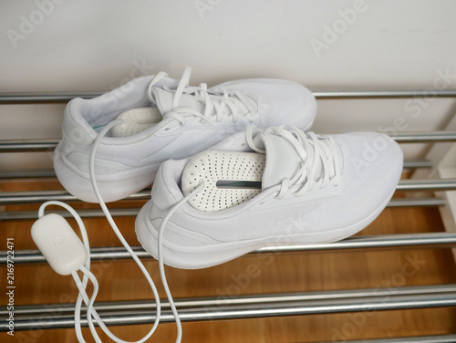 Electric shoes dryer. Pair of white wet sneakers drying with a plug-in boot warmer on a shoe rack. The concept of household technologies and smart gadgets.