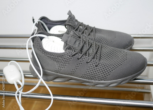 Electric shoes dryer. Pair of grey wet sneakers drying with a plug-in boot warmer on a shoe rack. The concept of household technologies and smart gadgets.