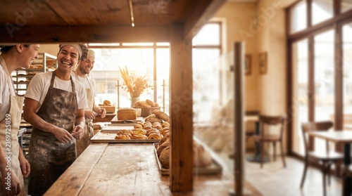Smiling male bakers working together in a cozy artisanal bakery, preparing fresh bread and pastries, representing teamwork and traditional craftsmanship.