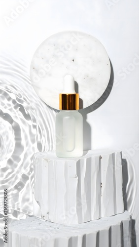 A luxurious serum bottle with a gold cap sits elegantly on a textured white pedestal, bathed in soft light and subtle water ripple reflections.