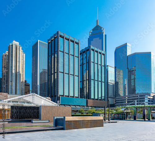 Contemporary high-rise architecture framing an open urban plaza in Wan Chai, Hong Kong, with reflective glass facades beneath an expansive blue sky.