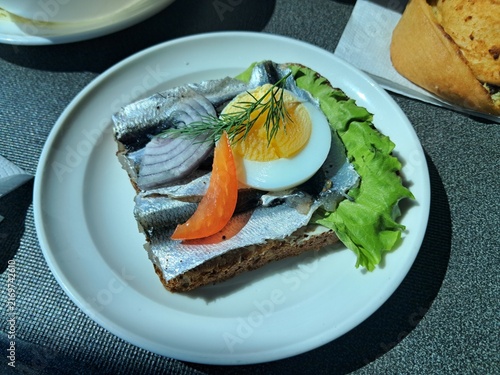 Traditional Baltic open face sandwich with salted herring, boiled egg slice, red onion, and lettuce on dark rye bread.