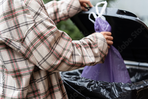Cuadro en lienzo Individual in a plaid shirt is seen disposing of a purple trash bag into a waste bin, highlighting the everyday act of waste management and environmental consciousness