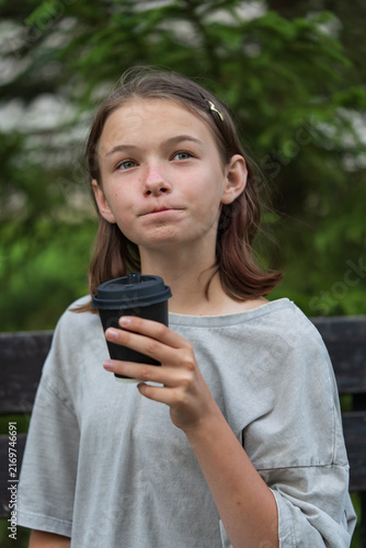 фотографія Young girl sipping from a paper cup while sitting outdoors