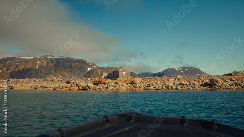 Foto The bow of a moving zodiac boat approaching a lonely wooden cabin on a rocky, ba