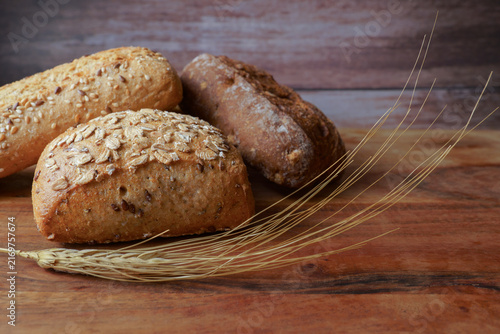 Variety of healthy whole grain bread rolls and spikelets of wheat on a dark wooden background, showcasing artisan bakery