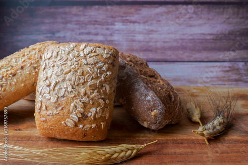 Assortment of healthy whole grain bread rolls and sourdough loaves on a wooden board, with rustic wheat ears