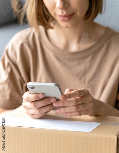 Close up of woman hands using smartphone for online shopping and tracking delivery package on cardboard box