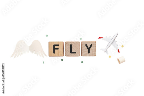 Fly word layout with wooden letter blocks, wooden wings, and toy airplane on white background; travel concept design, aviation typography, scratchpad style