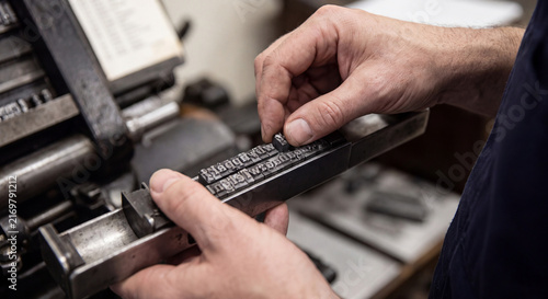 Close up view of the skilled hands of a printer carefully assembling metal movable type into a composing stick for traditional letterpress printing.