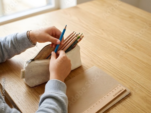 Hands Organizing Colored Pencils in a Pencil Case on Wooden Desk
