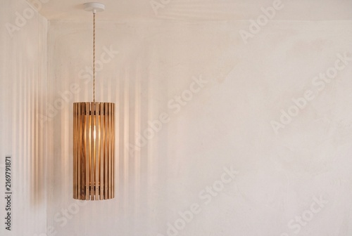 Timber lampshade casting linear shadows on a plaster wall