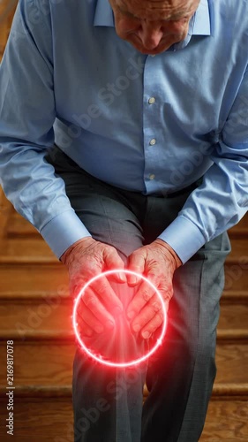 Senior man suffering from severe knee pain while walking down the stairs at home causing significant mobility issues