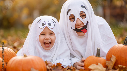 Laughing mother and daughter in cute ghost costumes making silly faces at camera for Halloween, ideal for festive family social posts and party banners.