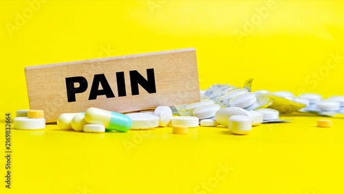 Wooden block with pain text surrounded by pills.