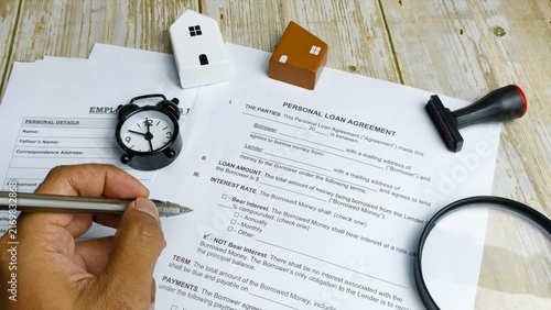 Hand filling personal loan agreement form with clock.