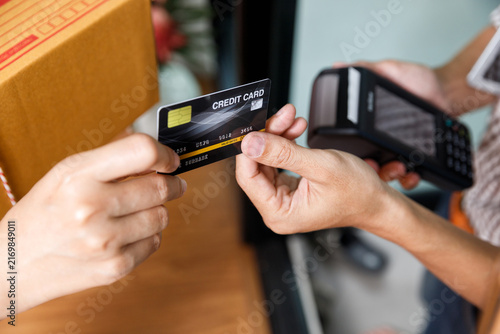 Customer paying by credit card on mobile POS terminal for cardboard box package delivery at home door. E-commerce shipping and digital payment concept.