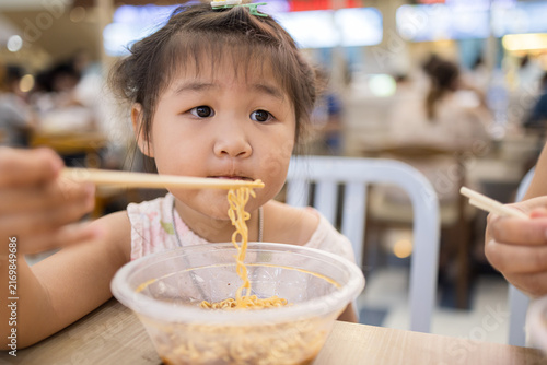 Canvastavla Cute Asian Girl Eating Instant Noodles with Chopsticks at a Restaurant,Close-up of an adorable little Asian girl enjoying a bowl of delicious instant noodles with chopsticks in a casual restaurant