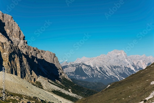 A stony alpine valley opens toward distant snow dusted Dolomite peaks under clear sky. Alpine hiking trails and panoramic mountain views for travel, tourism and wellness marketing