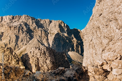 Jagged limestone Dolomite peaks rise against a deep blue sky beside a rocky pinnacle. Dramatic mountain wilderness for hiking, adventure travel and outdoor brand marketing