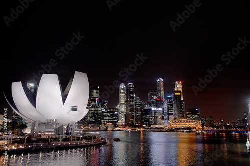 Singapore skyline at night with illuminated buildings and waterfront reflections.