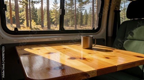 Wooden table inside camper van with coffee mug overlooking pine forest view