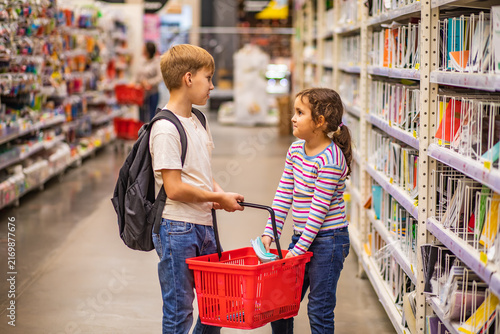 Cute little girl and teenager boy choosing school stationery in supermarket