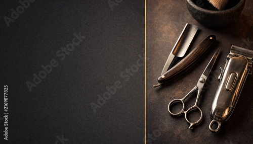 Vintage grooming tools including scissors, razor, clipper, brush, and comb arranged on a dark textured surface with generous copy space.