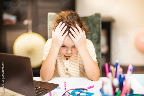 Little cute girl pupil at home making homework. Child studying online on laptop. Kid education.