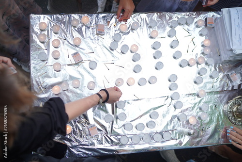 Foto Hands reach across a foil-covered table to light dozens of tealight candles at a somber community vigil, creating a quiet atmosphere of remembrance, solidarity, hope and collective tribute