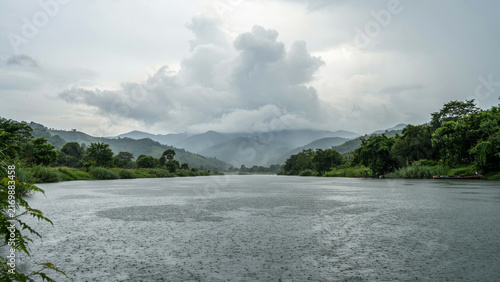 Calm mountain landscape with lush green forest and rocky riverbed under cloudy