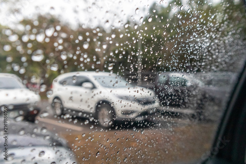 Raindrops on car side window glass with blurred white SUV vehicle parked outside