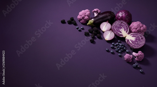 monochromatic food photography of purple vegetables and fruits including eggplant, purple cabbage, red onion, purple cauliflower, blackberries and blueberries arranged on a deep violet background 