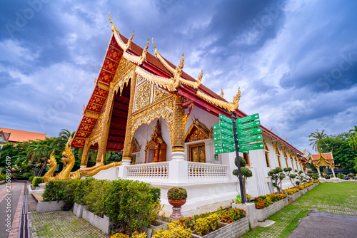 Golden Lanna style pavilion at Wat Phra Singh temple in Chiang Mai, Thailand under cloudy sky. Famous ancient Buddhist temple and cultural travel landmark. Horizontal orientation.